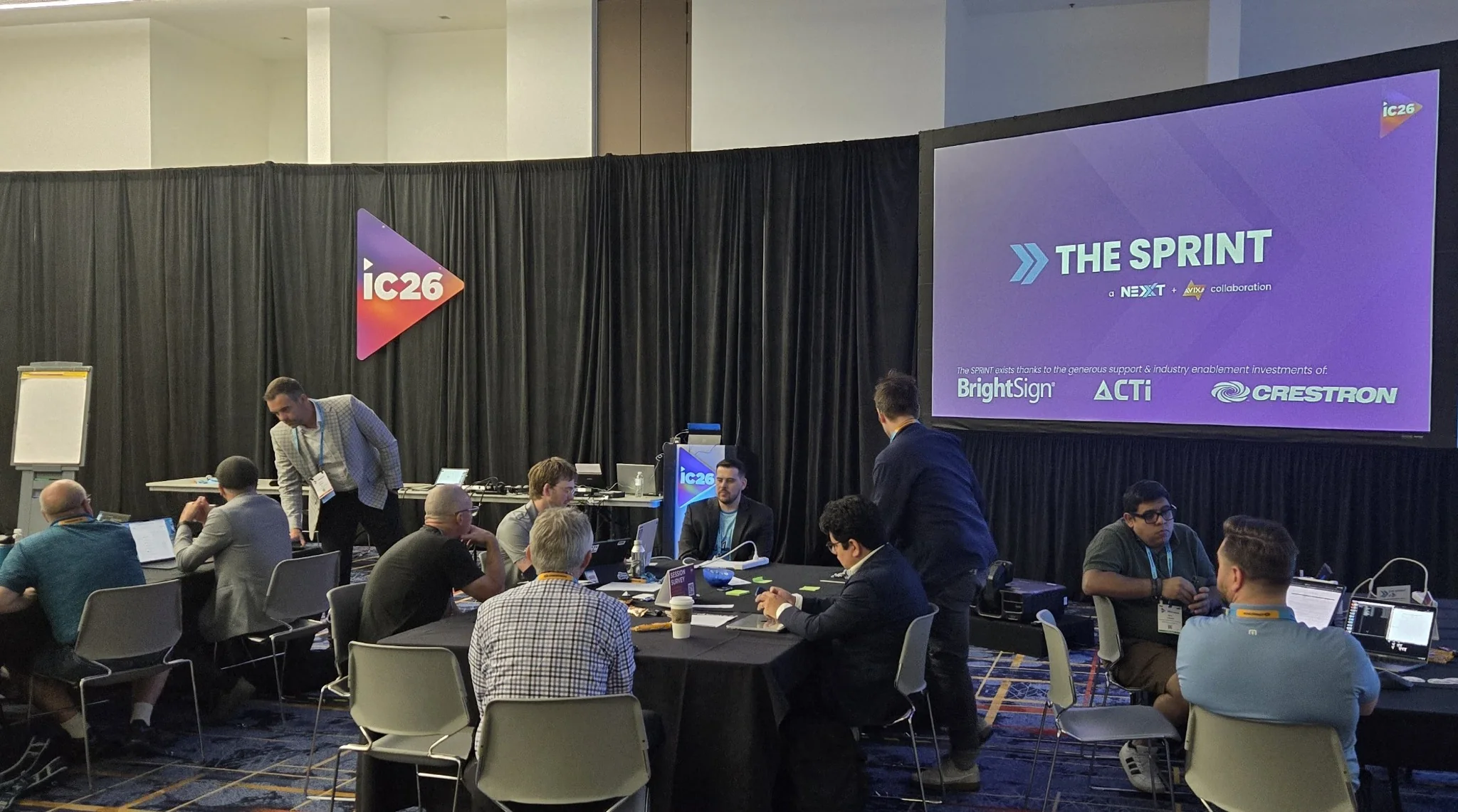 Participants working in small groups at The SPRINT during InfoComm 2026, with the program displayed on the room screen